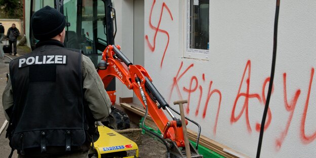 Polizist vor Fassade mit Hakenkreuzschmiererei Polizist vor Fassade mit Hakenkreuzschmiererei