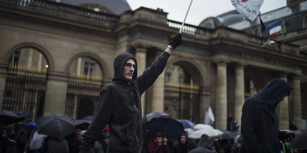 Ein Demonstrant hält eine Fahne hoch, im Hintergrund stehen weitere Menschen mit Regenschirmen