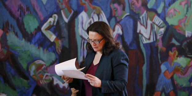 Andrea Nahles steht mit Dokumenten in der Hand vor einer mit Menschen bemalten Wand