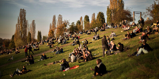 Menschen sitzen an einem Hang im Mauerpark in der Abendsonne Menschen sitzen an einem Hang im Mauerpark in der Abendsonne