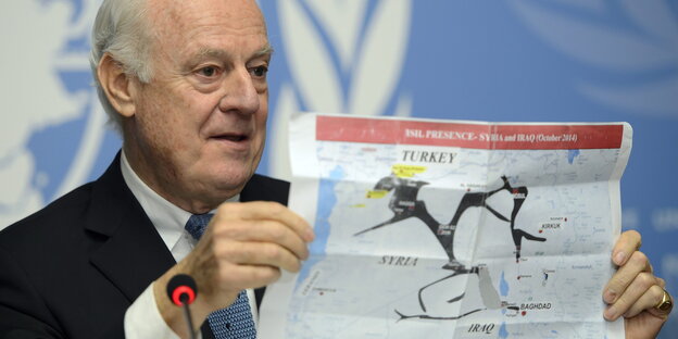 Staffan de Mistura hält einen Plan von Syrien und Irak in die Höhe, im Hintergrund sind Teile des UN-Logos zu sehen. Staffan de Mistura hält einen Plan von Syrien und Irak in die Höhe, im Hintergrund sind Teile des UN-Logos zu sehen.