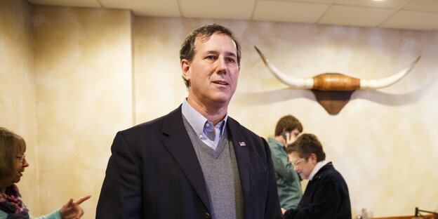 Rick Santorum steht in einem Raum. Hinter ihm an der Wand hängen Stierhörner, im Hintergrund einige Menschen Rick Santorum steht in einem Raum. Hinter ihm an der Wand hängen Stierhörner, im Hintergrund einige Menschen