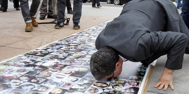 Mann kniet sich im Freien auf ein auf den Boden ausgebreitetes Banner mit Fotos nieder und küsst es. Mann kniet sich im Freien auf ein auf den Boden ausgebreitetes Banner mit Fotos nieder und küsst es.