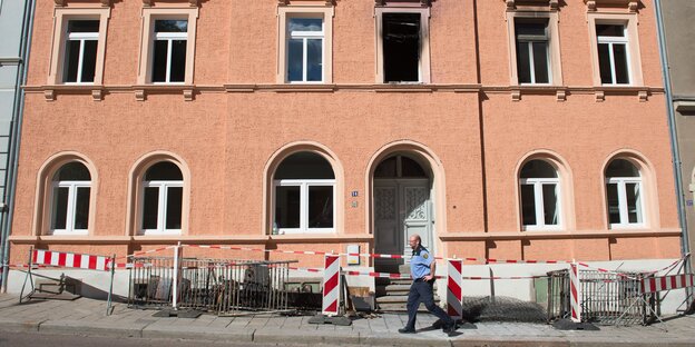 Ein Polizist läuft an einem mit Flatterband abgesperrten Haus vorbei