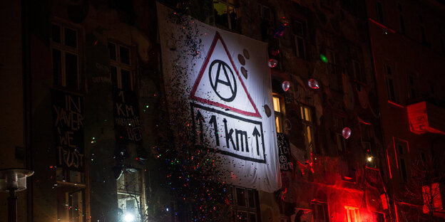 Ein Transparent mit der Aufschrift "1 KM" und einem Anarchiesymbol hängt an einem Gebäude Ein Transparent mit der Aufschrift "1 KM" und einem Anarchiesymbol hängt an einem Gebäude