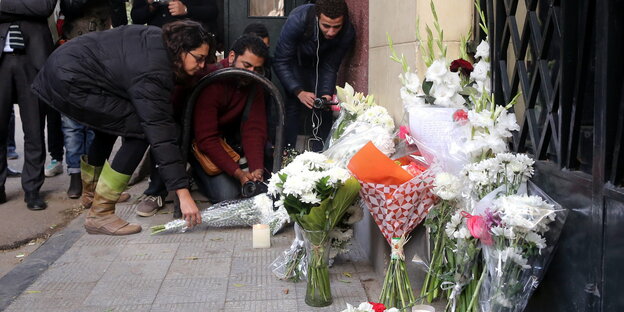 Menschen legen Blumen vor ein Eisentor