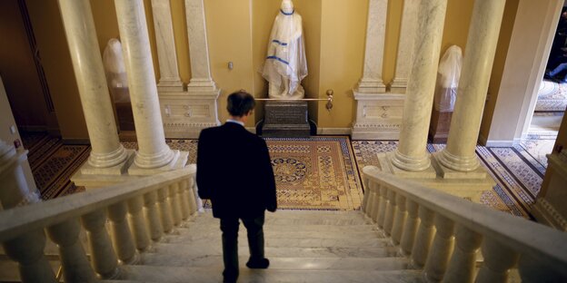 Mann geht die Treppe in einer Halle herunter. Man sieht von oben nur seine Rückseite. Unten stehen eingehüllte Statuen. Mann geht die Treppe in einer Halle herunter. Man sieht von oben nur seine Rückseite. Unten stehen eingehüllte Statuen.