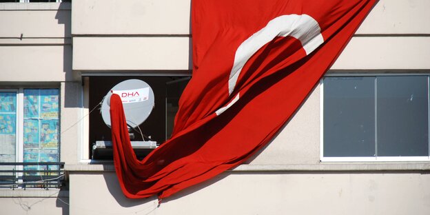 Ein Balkon, an dem eine Satellitenschüssel angebracht ist. Daneben hängt eine türkische Flagge. Sie hat sich an der Schüssel verheddert.