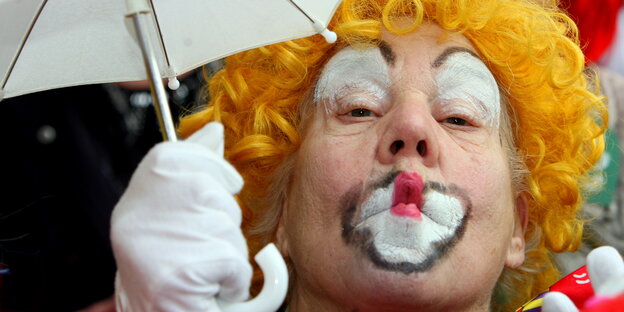 Zum Clown geschminkter Mann hält einen Regenschirm und wirft ein Küsschen und Richtung des Betrachters. Zum Clown geschminkter Mann hält einen Regenschirm und wirft ein Küsschen und Richtung des Betrachters.