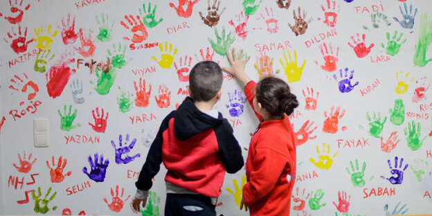 Zwei Kinder stehen vor einer Wand voller bunter Händeabdrücke Zwei Kinder stehen vor einer Wand voller bunter Händeabdrücke