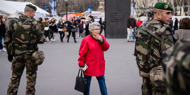 Eine ältere Dame in Rot zwischen zwei Soldaten auf den Champs-Élysées in Paris Eine ältere Dame in Rot zwischen zwei Soldaten auf den Champs-Élysées in Paris