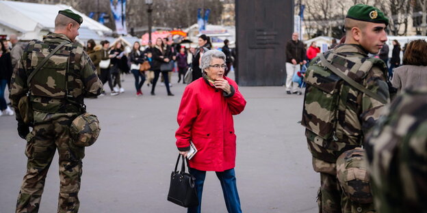 Eine ältere Dame in Rot zwischen zwei Soldaten auf den Champs-Élysées in Paris