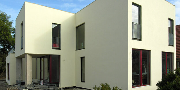 Ein weißer modernistischer Neubau mit roten Fensterrahmen vor blauem Himmel