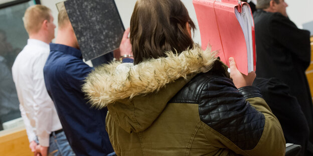 Eine Frau und zwei Männer sind von hinten zu sehen, sie verstecken ihre Gesichter hinter Aktenordnern. Eine Frau und zwei Männer sind von hinten zu sehen, sie verstecken ihre Gesichter hinter Aktenordnern.