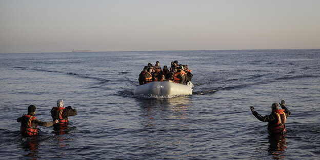 Ein Schlauchboot mit Flüchtlingen in Rettungswesten fährt auf Menschen zu, die im Wasser stehen Ein Schlauchboot mit Flüchtlingen in Rettungswesten fährt auf Menschen zu, die im Wasser stehen