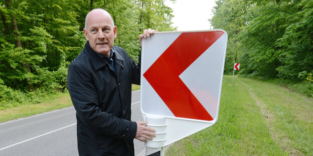 Der grüne Verkehrsminister Hermann steht an einer Landstraße und befestigt einen Leitpfosten. Der grüne Verkehrsminister Hermann steht an einer Landstraße und befestigt einen Leitpfosten.