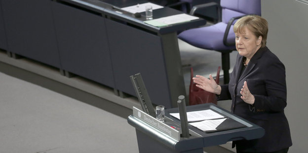Angela Merkel steht mit erhobenen Händen vor einem Rednerinnenpult