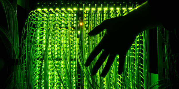 eine Hand vor einem Verteilerpunkt, in dem grün leuchtende Glasfaserkabel zusammenlaufen eine Hand vor einem Verteilerpunkt, in dem grün leuchtende Glasfaserkabel zusammenlaufen