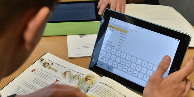 Ein Schüler arbeitet gleichzeitig mit einem Schulbuch und einem Tablet. Ein Schüler arbeitet gleichzeitig mit einem Schulbuch und einem Tablet.