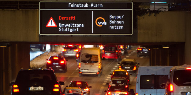 Autos fahren auf einer mehrspurigen Straße, darüber ein Schild, das den Feinstaub-Alarm anzeigt Autos fahren auf einer mehrspurigen Straße, darüber ein Schild, das den Feinstaub-Alarm anzeigt