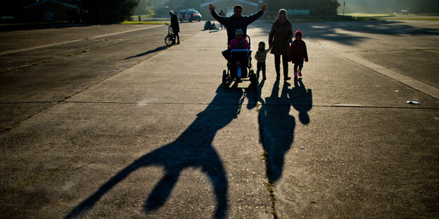 Eine Familie läuft nebeneinander im Sonnenschein. Man sieht ihre Schatten auf dem Boden Eine Familie läuft nebeneinander im Sonnenschein. Man sieht ihre Schatten auf dem Boden