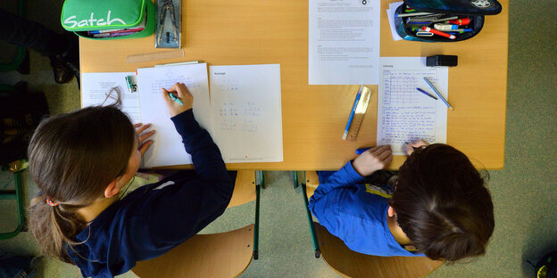 Ein Schüler und eine Schülerin sitzen an einem Tisch und arbeiten. Das Bild zeigt sie von oben. Ein Schüler und eine Schülerin sitzen an einem Tisch und arbeiten. Das Bild zeigt sie von oben.