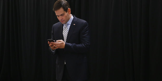 Ein Mann im Anzug, es ist Marco Rubio, schaut auf sein Handy, das er in den Händen hält