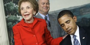 Nancy Reagan legt ihre Hand auf die Schulter von Obama., der gerade den Vertrag unterschreibt.