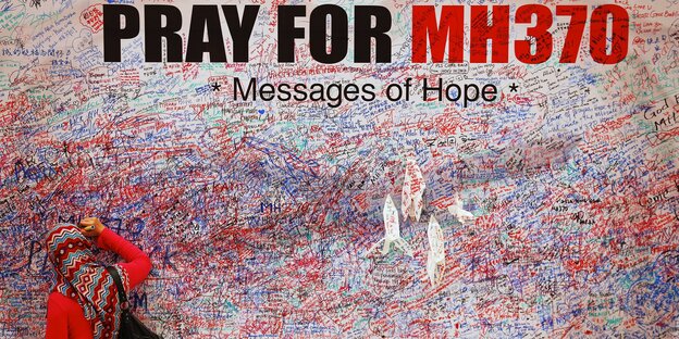 Eine Frau mit Kopfstuch schreibt etwas an eine vollgeschriebene Wand, die mit "Pray for MH370. Messages of Hope" überschrieben ist Eine Frau mit Kopfstuch schreibt etwas an eine vollgeschriebene Wand, die mit "Pray for MH370. Messages of Hope" überschrieben ist