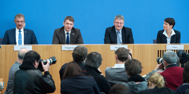 AfD-Politiker sitzen auf einem Podium, davor stehen Fotografen. AfD-Politiker sitzen auf einem Podium, davor stehen Fotografen.