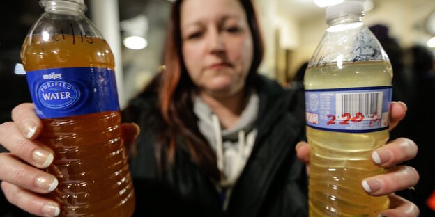 Eine Frau hält zwei Plastikflaschen, die eine bräunliche Flüssigkeit enthalten, in den Händen