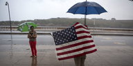 ein Mann mit Regenschirm in eine US-Fahne gehüllt