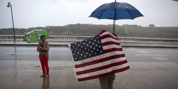 ein Mann mit Regenschirm in eine US-Fahne gehüllt ein Mann mit Regenschirm in eine US-Fahne gehüllt