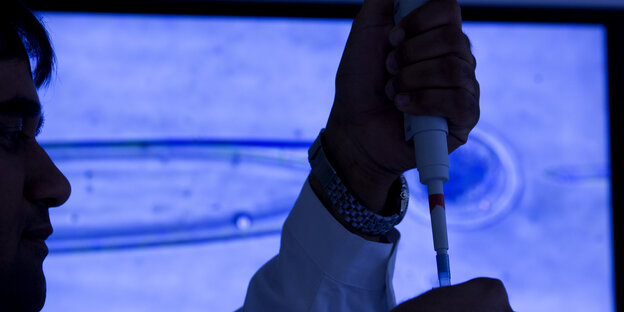 Ein Mann hält eine Pipette in der Hand, im Hintergrund ein Bild mit Eiszelle Ein Mann hält eine Pipette in der Hand, im Hintergrund ein Bild mit Eiszelle