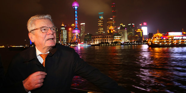 Präsident Gauck auf einem Boot oder am Ufer eines Flusses, mit Stadtkulisse samt Fernsehturm im Hintergrund. Es ist Nacht