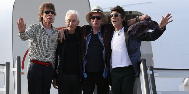 Die vier Mitglieder der Rolling Stones stehen oben auf einer Gangway vor der Eingangstür zum Flugzeug und winken Die vier Mitglieder der Rolling Stones stehen oben auf einer Gangway vor der Eingangstür zum Flugzeug und winken