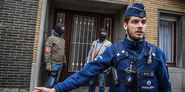 Zwei vermummte Männer stehen in einer Tür, vor ihnen ein Polizeibeamter in blauer Uniform Zwei vermummte Männer stehen in einer Tür, vor ihnen ein Polizeibeamter in blauer Uniform