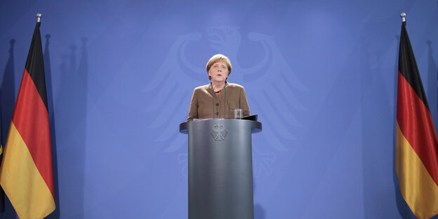 Eine Frau, Angela Merkel, steht an einem Pult, rechts und links von ihr Deutschland-Fahnen Eine Frau, Angela Merkel, steht an einem Pult, rechts und links von ihr Deutschland-Fahnen