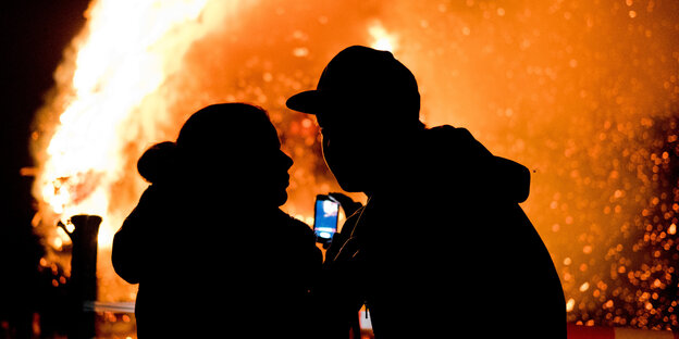 zwei Menschen vor Feuer mit Smartphone in den Händen zwei Menschen vor Feuer mit Smartphone in den Händen