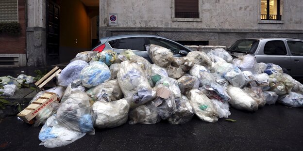 Aufeinandergestapete Mülltüten liegen vor einem Auto auf der Straße Aufeinandergestapete Mülltüten liegen vor einem Auto auf der Straße