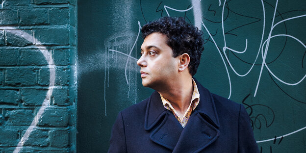 Der Autor Neel Mukherjee seitlich im Profil vor einer Wand mit Graffitti Der Autor Neel Mukherjee seitlich im Profil vor einer Wand mit Graffitti