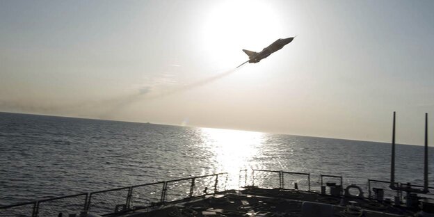 Ein Kampfflugzeug fliegt über einem Schiff vor der Sonne Ein Kampfflugzeug fliegt über einem Schiff vor der Sonne