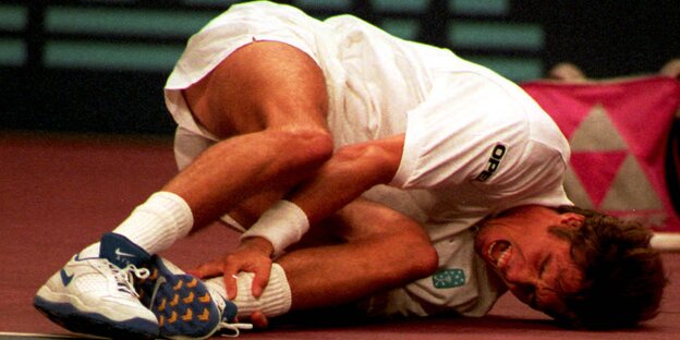 Michael Stich liegt im weißen Tennisdress am Boden und hält sich schreiend den Knöchel Michael Stich liegt im weißen Tennisdress am Boden und hält sich schreiend den Knöchel