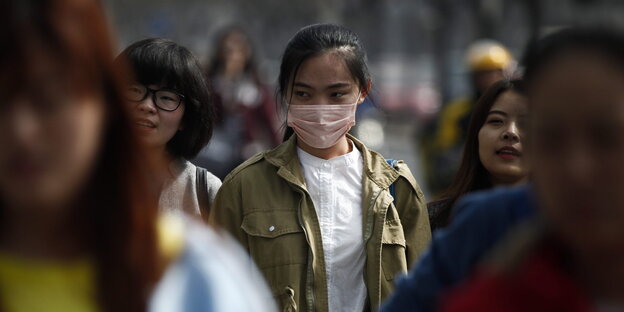 Eine Frau mit Atemschutzmaske zwischen Passanten in Peking Eine Frau mit Atemschutzmaske zwischen Passanten in Peking