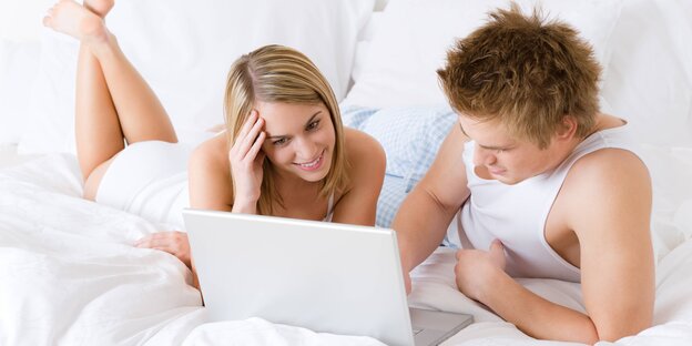 Eine Frau und ein Mann liegen mit Laptop in einem weißen Bett Eine Frau und ein Mann liegen mit Laptop in einem weißen Bett