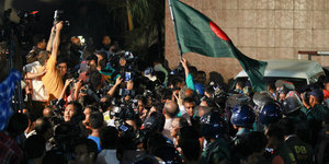 Eine Menschengruppe mit Flagge, umringt von Fotografen und Polizisten