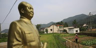 goldene Mao-Statue, dahinter Felder und ein Haus mit Giebeldach