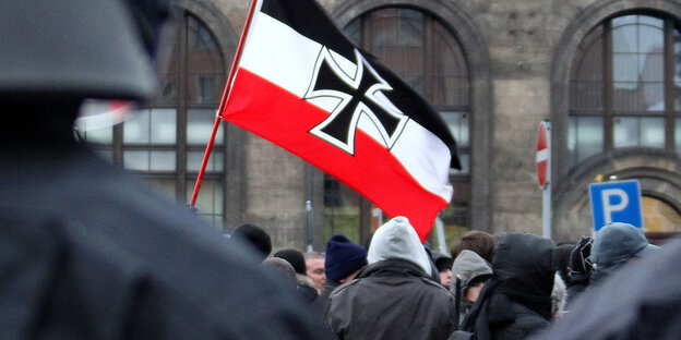 Hinter Polizisten stehen vermummte Rechte, eine Reichkriegsflagge mit einem Eisernen Kreuz weht darüber Hinter Polizisten stehen vermummte Rechte, eine Reichkriegsflagge mit einem Eisernen Kreuz weht darüber