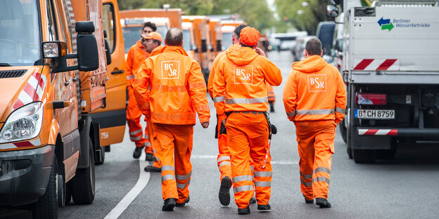 Männer in orangefarbener Kleidung neben Müllautos Männer in orangefarbener Kleidung neben Müllautos