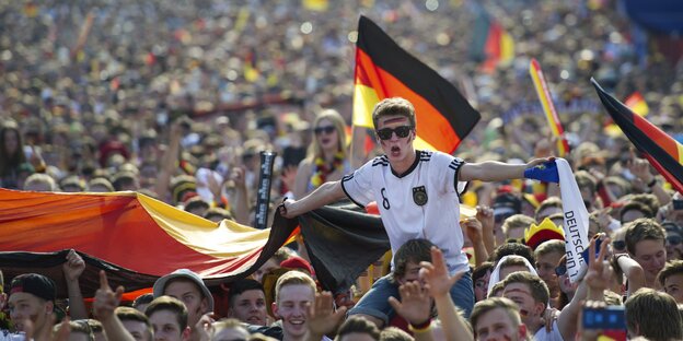 Fußballsfans halten viele Deutschlandflaggen hoch, tragen Sonnenbrillen und gröhlen Fußballsfans halten viele Deutschlandflaggen hoch, tragen Sonnenbrillen und gröhlen